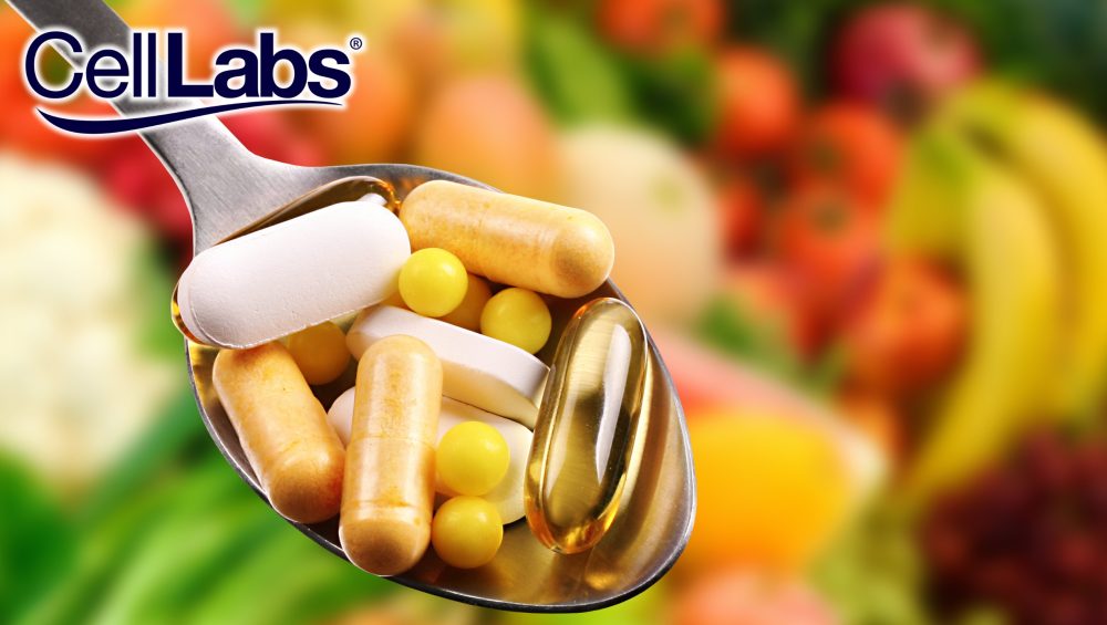 Image of spoon with different health supplement capsules with a background of fruits and vegetables.